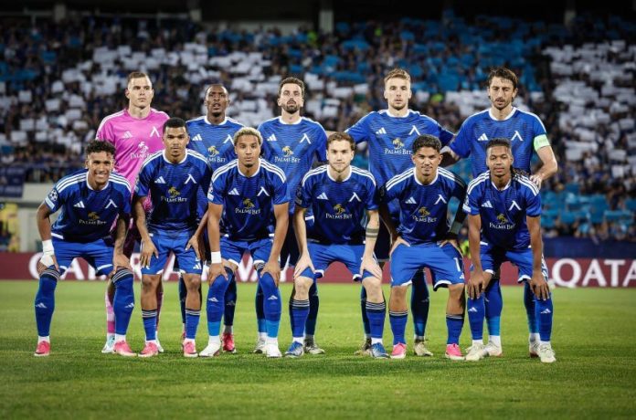 Soccer team in blue uniforms posing for a pre-match group photo on the field.