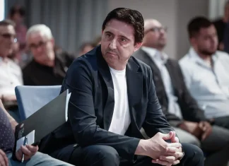 Боримиров разкри голямата трансферна цел на Левски Man in a dark blazer and white shirt sits in an audience, hands clasped, listening attentively at a conference.
