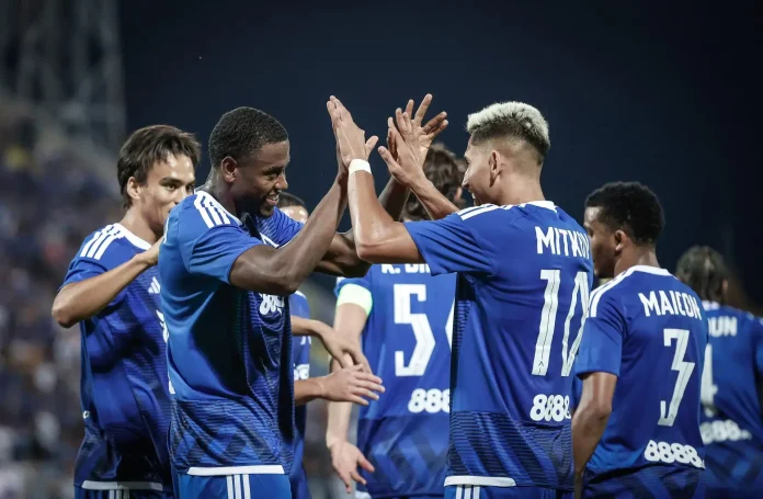 Soccer teammates in blue jerseys high-fiving in celebration on the field, numbers 5 and 7 visible on their backs.