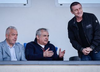 Лъчезар Танев: На Левски му липсва класен централен нападател Three men in a dugout: two seated on blue seats, one standing and smiling at the right.