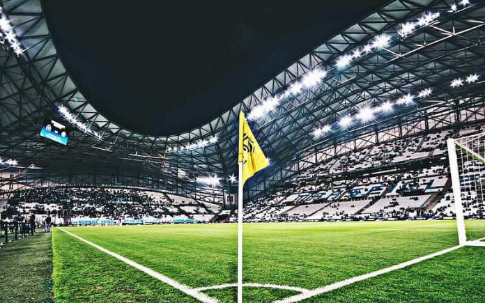 Soccer stadium at night with bright floodlights and a yellow corner flag in the foreground.