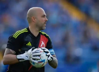 Ники Михайлов за загубата на баща си и новия инвеститор в Левски Bald male soccer goalkeeper wearing a black jersey with yellow stripes, holding a ball in white gloves on a field.