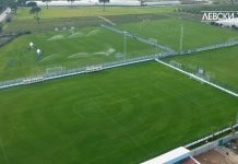 Нов вариант за базата на Левски Aerial view of a soccer field being watered by multiple sprinklers, with players and staff on the nearby practice area and dugouts along the sideline.
