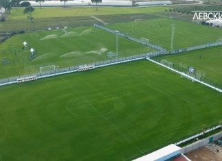 Нов вариант за базата на Левски Aerial view of a soccer field being watered by multiple sprinklers, with players and staff on the nearby practice area and dugouts along the sideline.