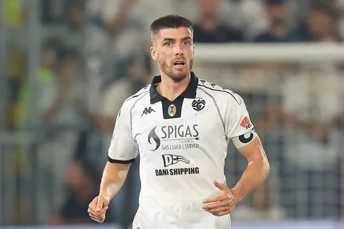 Male soccer player in a white jersey running on the field during a match, stadium blurred in the background