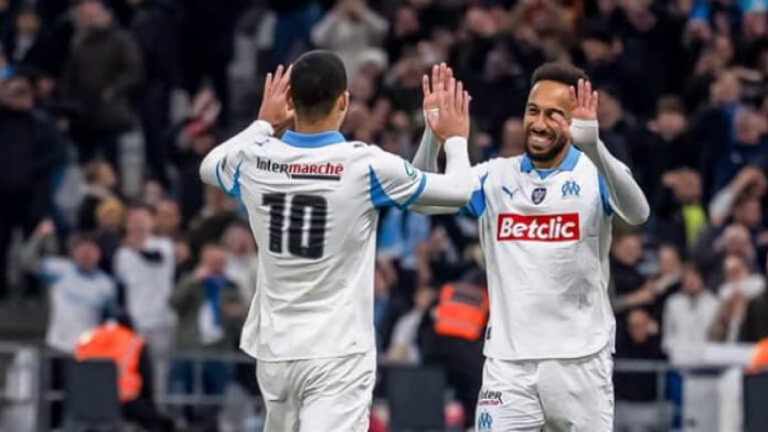 Two soccer players in white Olympique de Marseille jerseys high-fiving on the field during a match, Betclic sponsor visible on chest.