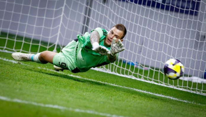 Soccer goalkeeper in green dives horizontally to save a ball near the goal line.