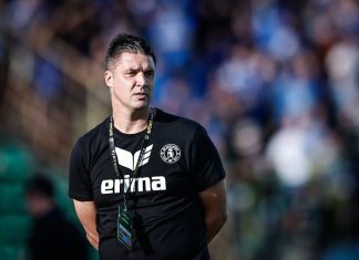 Тодор Симов: Можехме да вземем и трите точки срещу Левски Male sports coach in a black Erima shirt with a lanyard and badge, standing on a field with a blurred stadium crowd behind him.