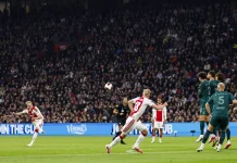 Аякс се издъни у дома срещу НЕК Soccer match action: players in red-and-white and teal kits chase a ball near the penalty area with a packed stadium crowd in the background