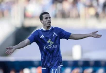 Акрам Бурас: профил на футболиста Soccer player in a blue kit with arms outstretched during a match, celebrating on the field.