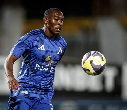 Алдаир – пълен профил и професионален път Male soccer player in a blue kit chasing a colorful ball on a field during a night match, focused and athletic posture.
