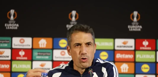 Бранител може да остане извън групата за Черно море Man in a navy jacket speaks at a press conference, seated behind a table with a microphone and a colorful sponsor backdrop behind him.
