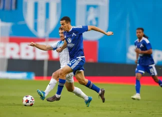 Добри новини за Левски: Акрам Бурас е близо до завръщане Blue-team player runs with the ball in a midfield sprint while a white-team defender closes in on a sunny stadium field.