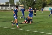 Дубълът на Левски надви Пирин в Разлог Soccer players in blue uniforms contest the ball on a grass field as a tackler in black attempts to stop them on the ground nearby