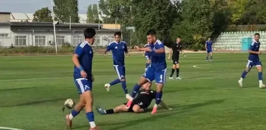 Дубълът на Левски надви Пирин в Разлог Soccer players in blue uniforms contest the ball on a grass field as a tackler in black attempts to stop them on the ground nearby