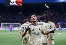 Евертон Бала: Не бяхме перфектни, но показахме какво може Левски! Soccer player in beige striped kit celebrates with fists raised on the field as teammates stand behind him and fans cheer in the stands.