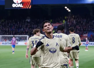 Евертон Бала: Не бяхме перфектни, но показахме какво може Левски! Soccer player in beige striped kit celebrates with fists raised on the field as teammates stand behind him and fans cheer in the stands.