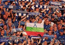 Фенове на Левски с призив преди НЕК: Без излишно напрежение и драми Crowd of football fans in blue and white, holding scarves; a flag with white-green-red and a blue emblem visible in the center