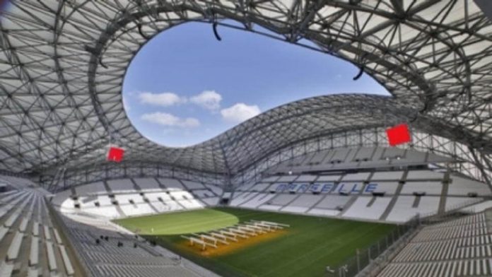 Interior of a modern domed stadium with a large circular skylight, green field, and white seating surrounding it