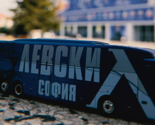 Фенски артикул на Левски излезе по-скъп от тези на Реал Мадрид и Ливърпул Blue toy bus with bold Cyrillic lettering on a cobblestone street; blurred city background.