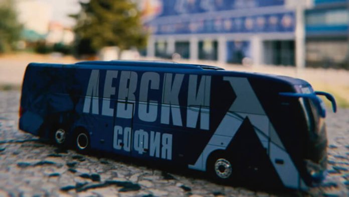 Blue toy bus with bold Cyrillic lettering on a cobblestone street; blurred city background.