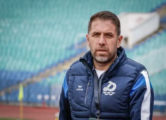 Георги Чиликов преди сблъсъка с Левски: Дунав няма да се предаде без битка Portrait of a man with short brown hair and a beard wearing a navy quilted jacket with a white emblem, standing on a track in a stadium with green seats in the background.
