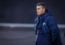 Георги Костадинов: Левски показа класа, характер и европейско самочувствие Side profile of a male coach in a blue puffer jacket standing on a field, looking to the right.