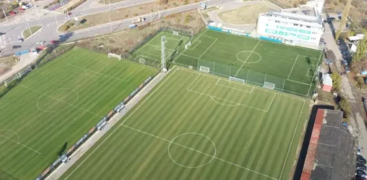 Големи промени на „Герена“! Левски търси две бази заради строежа на новия стадион Aerial view of three soccer fields with well-marked lines and a white multi-story stadium at the top-right corner.