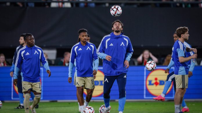 Soccer players in blue training kits warming up on a field with balls in the air and at their feet.