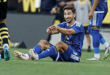 Груич влиза сред титулярите на Левски за гостуването на НЕК Soccer player in a blue kit sitting on the grass and smiling, gesturing with his arms during a match, with a opponent in yellow and black nearby.