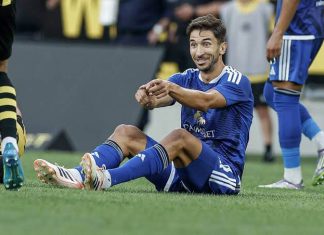 Груич влиза сред титулярите на Левски за гостуването на НЕК Soccer player in a blue kit sitting on the grass and smiling, gesturing with his arms during a match, with a opponent in yellow and black nearby.