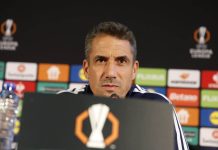 Хулио Веласкес е най-скъпоплатеният треньор в Първа лига Sports coach at a press conference speaking into a microphone, backdrop with sponsor boards and a trophy logo on the podium