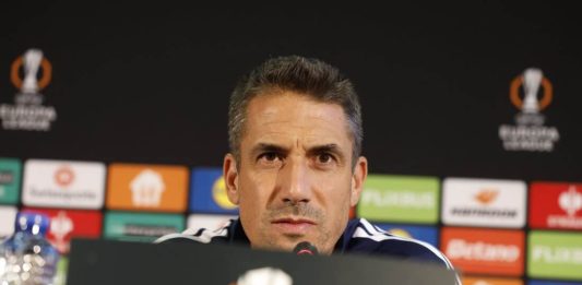 Хулио Веласкес е най-скъпоплатеният треньор в Първа лига Sports coach at a press conference speaking into a microphone, backdrop with sponsor boards and a trophy logo on the podium