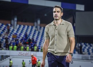 Хулио Веласкес празнува 45 години Man in a beige short-sleeve polo and navy pants walks across a stadium field with blurred spectators in the stands behind him.