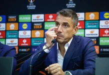 Хулио Веласкес преди НЕК: Левски няма да променя стила си дори срещу Реал Мадрид Man in a blue suit at a press conference, touching his eye while speaking into a microphone, backdrop of sponsor logos.