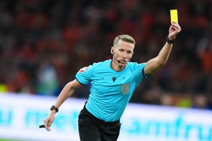 Soccer referee in light blue shirt showing a yellow card during a match.