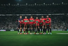 Кадрови проблеми в НЕК Ниймеген преди Левски A soccer team in red jerseys posing for a group photo on a well-lit stadium pitch, UEFA signage visible in the background.