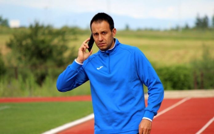Man in a blue athletic jacket on a running track, talking on a smartphone.