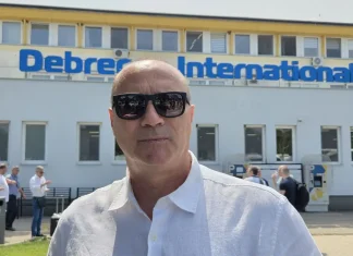 Кокала: Левски пак ще е шампион Man in a white shirt wearing dark sunglasses stands in front of a building with a blue 'Debrecen International' sign above the windows.