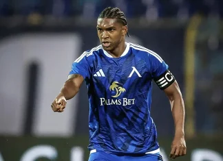 Кристиан Макун: биография, кариера и статистика Soccer player in blue kit with 'Palms Bet' sponsor, wearing captain's armband, pointing forward on the field.