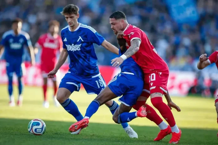 Soccer players in blue and red vie for the ball on a green field during a match