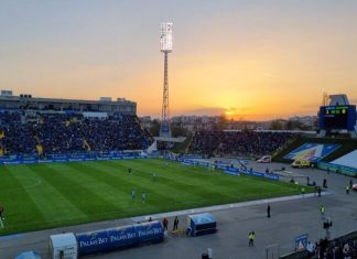 Левски има специален спомен от 15 октомври Football stadium at sunset with players on the green pitch and a large crowd in blue stands.