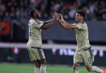 Левски измъкна точка в Нидерландия след здрава битка с НЕК Ниймеген Two soccer players in beige kits high-five each other on the field, celebrating with a cheering crowd in the background.