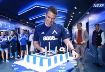 Левски изненада Веласкес за рождения му ден Man in a blue team jersey cuts a large blue-and-white striped cake while teammates applaud in a hallway.