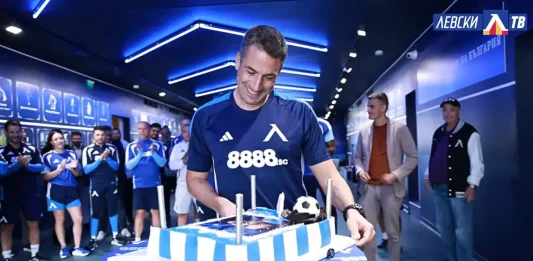 Левски изненада Веласкес за рождения му ден Man in a blue team jersey cuts a large blue-and-white striped cake while teammates applaud in a hallway.