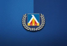 Левски надъха феновете си за гостуването в Ловеч с любопитно видео и музикален поздрав Emblem with a blue shield, white triangular arch, red and yellow bars, flanked by gold laurel branches, and ‘1914’ beneath on a blue textured background, resembling a union logo