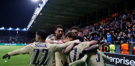Левски направи това, което никой български отбор не успя Soccer players in beige uniforms huddle together in celebration on the pitch as spectators cheer in the stands in the background.