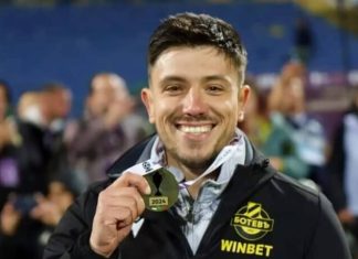 Левски с нов скаут Smiling man holding a gold medal labeled 2024 after winning a competition, wearing a jacket with WINBET logo.