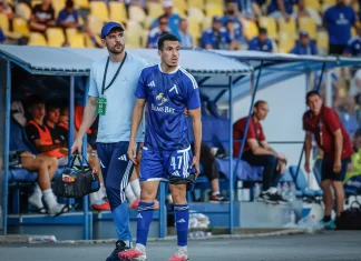 Левски няма да бърза с Бурас Soccer player in blue kit (number 47) stands by the dugout with a staff member carrying a medical bag, stadium seating in yellow behind.