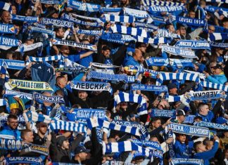 Левски обяви как ще компенсира феновете с пакетни билети за Лига Европа Crowd of football fans primarily in blue and white, holding scarves and cheering in a stadium stands.